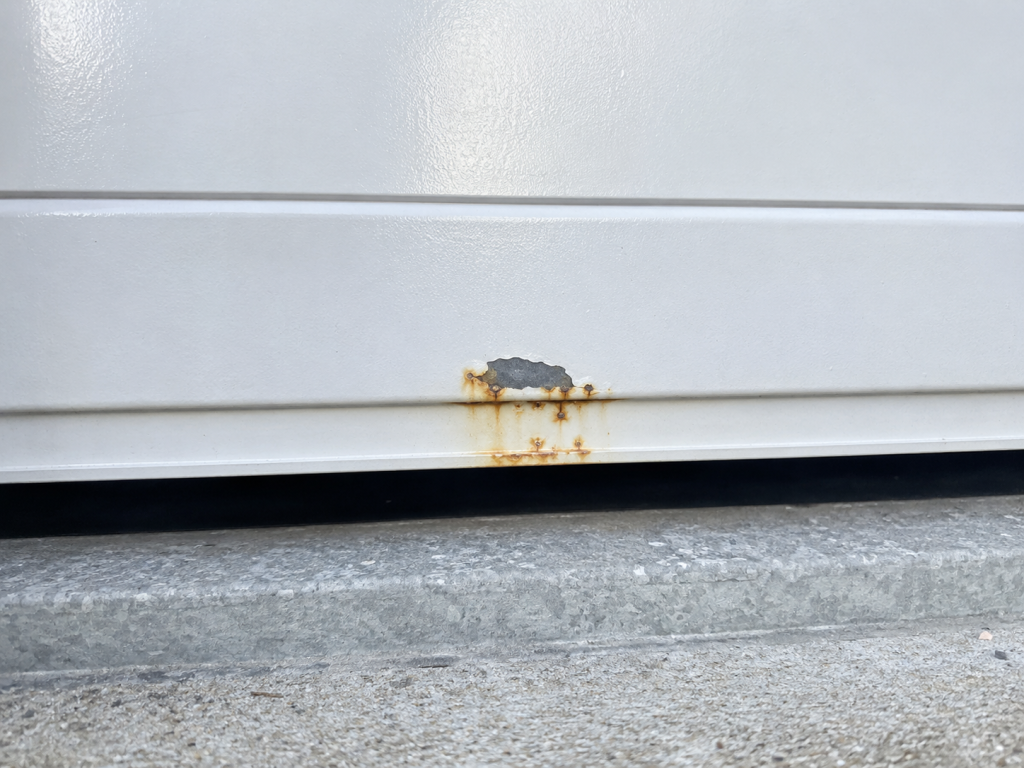 Corrosion en partie basse d'une porte de garage en acier laqué, à partir d'un éclat de revêtement